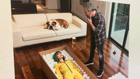 A picture of a piece of art generated by AI. There is a man in jeans and a checked shirt standing over a woman with green hair in a yellow jumpsuit in a box. There is a bulldog lying on the sofa.