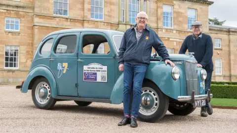 Sean Spencer/Hull News & Pictures Ltd Two men smile next to a blue vintage car, which is parked in front of a manor house.