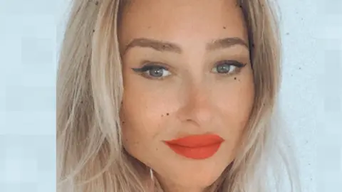 Joanna Derkacz smiles at the camera in a close-up photo. She has long, blonde hair and wears eye make-up and red lipstick.