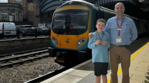 Nathaniel Briggs of the Transpennine Express and Steve Whitehead, the lead driver, stand on a platform in front of a train 