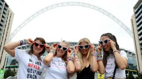 Reuters Infront of a backdrop of the arch at Wembley Stadium, four Taylor Swift fans post with their heart-shaped sunglasses and T shirts featuring song lyrics and phrases coined by the American singer. 