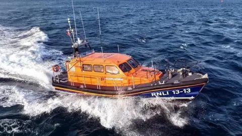 Swanage all-weather lifeboat in Swanage Bay. The sea is almost black with white waves surrounding the orange and navy blue lifeboat.