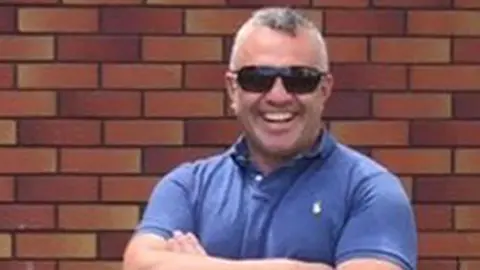 Sergeant Matt Ratana in casual clothes smiling in front of a red brick wall