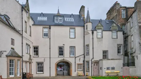 The Chambers Institution in Peebles viewed from an internal courtyard - a four-storey building of a greyish-brown colour with numerous windows and an arched doorway