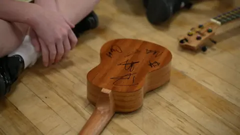 small brown ukulele with several autographs on the back.