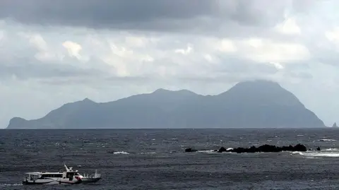 Akuseki Island, one of the main islands for tourists visiting Tokara, is seen in the horizon. A small ferry is in the sea, in the foreground
