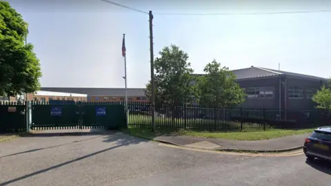 Google The Downs School in Newbury - a single storey building, the view of which is slightly obscured by two trees and closed gates