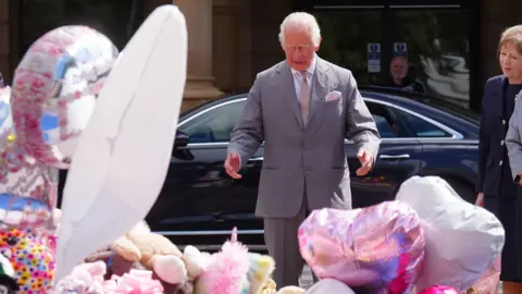 PA Media King Charles III bekijkt bloemen en gedenktekens voor de slachtoffers van de mesaanvallen in Southport buiten het stadhuis van Southport