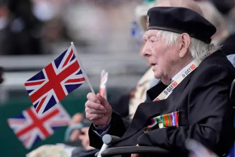 Andrew Matthews/PA Media A Normandy veteran waves a flag