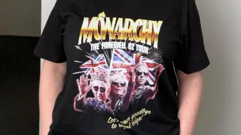 Australian Republican Movement A woman wearing the Australian Republican Movement merch. It's a t-shirt which reads "Monarchy the farewell Oz tour" and "Let's wave goodbye to Royal reign!". It features edited photos of King Charles in a crown, Queen Camilla and Prince William. All three are wearing sunglasses.
