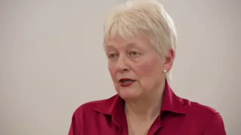 A woman with white short hair, a red shirt and red lipstick.