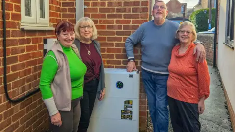 Dilton Memorial Hall Three women and a man stand outside a red brick building, next to a white box that is part of a solar panel installation.
