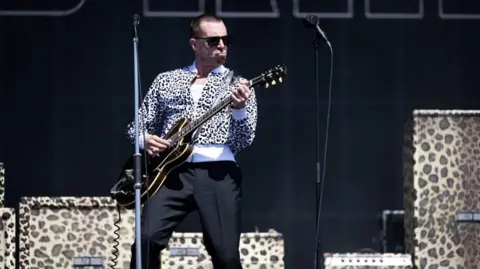 a man in a leopard print top with a guitar