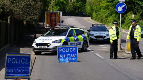 Two police officers next to blue signs reading 'police slow, road closed'