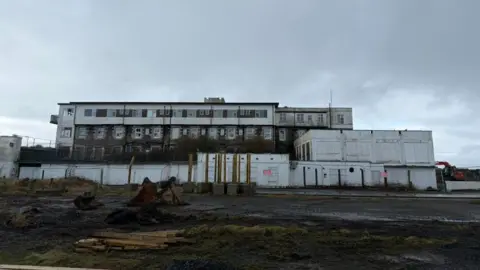 FRANK SCHUENGEL The hotel now, a large white building which is rusting, there is fencing around it.