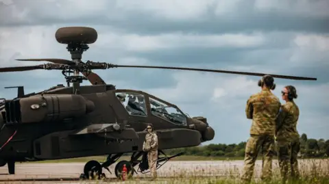 Soldiers in the foreground with an Apache helicopter in the background