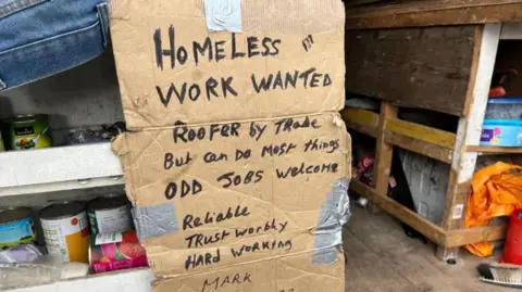A photo of a piece of cardboard with the words "work wanted - roofer by trade" which Mark Hamblin had in the back of his van.
