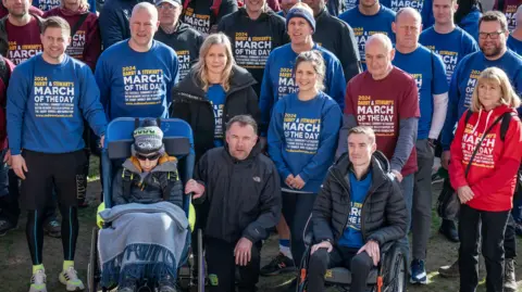 PA Media Stewart and Darby and pictured in a group with other walkers from last year's March of the Day. Rob Burrow sits in a chair next to Stewart. 