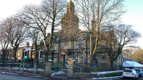 Trees mask a Victorian building in Yorkshire stone with a blue winter sky behind it.