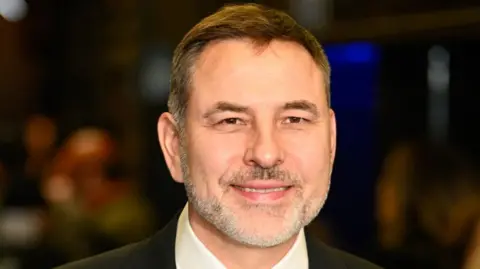 A close up photo of David Walliams in a dark suit 
