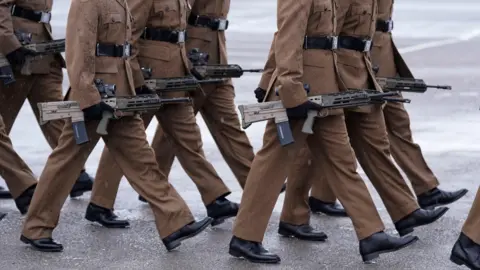 A shot of members of the armed forces marching and carrying rifles