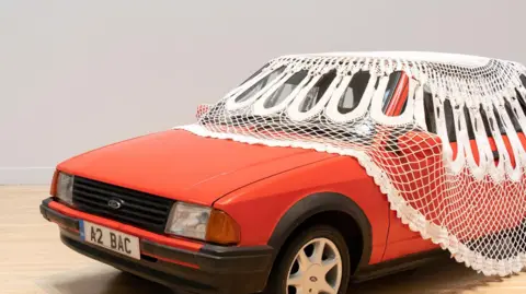 A red car with a doily over, part of Jasleen Kaur's exhibition