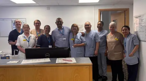 South Tyneside and Sunderland NHS Foundation Trust Ben Banerjee with nine of his hospital colleagues. They are standing in a reception area behind a wooden desk.