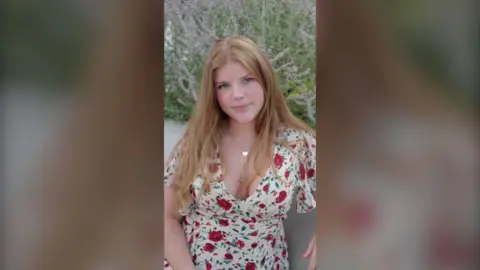 A young woman with long blonde hair wearing a flowery dress.