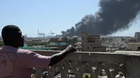 AFP / Getty Images watch a man while a large column of smoke rises on the city horizon.