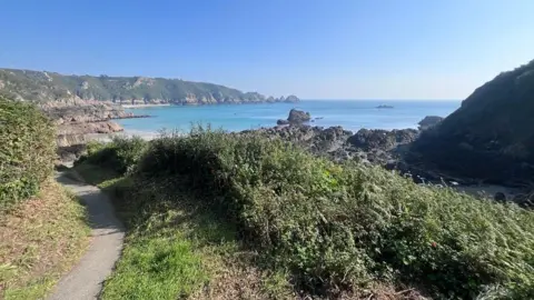 BBC A wide bag on a sunny day, framed by high granite cliffs and green vegitation.