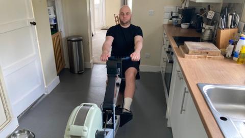 Tom Mould in a rowing machine at home in his kitchen