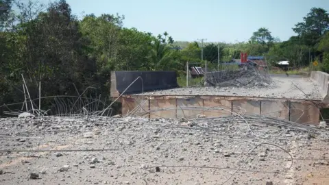 A bridge with a gaping hole in the centre, over the Me Teuk river. Thailand bombed the Chinese-built expanse in December
