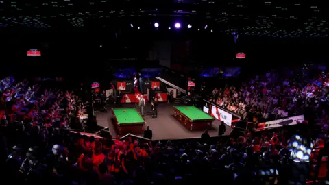 Getty Images Two snooker tables sit side by side in a theatre packed with spectators.
