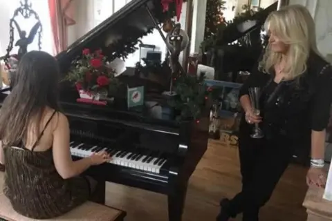 Julie Read A young girl sat at a black baby grand piano with her back to the camera and Bonnie Tyler standing beside her.