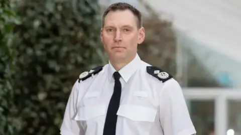 Avon and Somerset Police Det Ch Con Reilly, pictured wearing his uniform including a white shirt, black tie and two black and silver shoulder patches. 