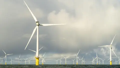 PA Media Large three-bladed white turbines out at sea. The water is dark and there are thick, dark clouds in the sky above.