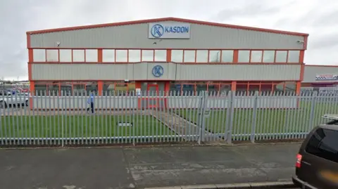 A grey corrugated industrial building with red framing and the letter K circled in the colour blue as its logo. A sign says Kasdon in capital letters  