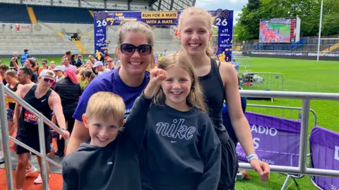 A woman and three children, all smiling. They are stood in an outdoor stadium setting. 