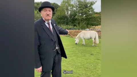 Beamish Ian Bean, wearing his 1900s costume, is pointing at a horse. A caption below reads: "Smol".