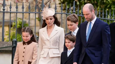 William and Kate walking with their three children looking down as they walk 