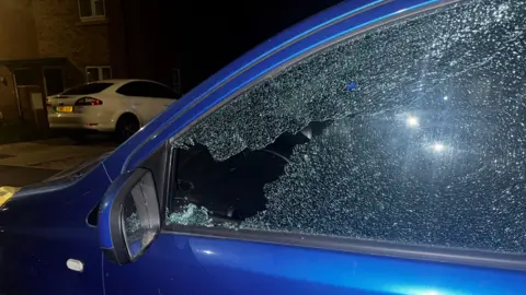 Supplied Image of a blue car with a smashed window. The picture is taken at night.