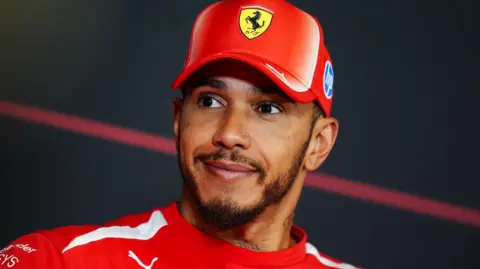 Getty Images Lewis Hamilton is smiling while dressed in red