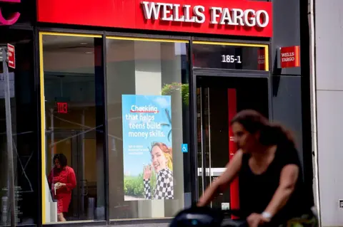 A woman pushes a pram in front of a Wells Fargo bank branch