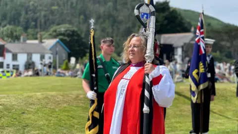 The bishop who is wearing red and white robes and it carrying a crozier.