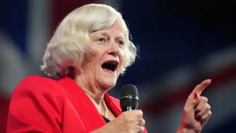 Getty Images Close-up of Ann Widdecombe, wearing a red blazer, speaking into a microphone, with her hand raised.