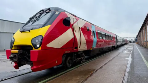 CrossCountry A refurbished CrossCountry train on some tracks at what appears to be a train depot. The train is painted red with a white cross near the driver's door.