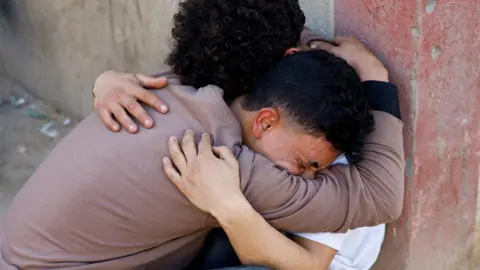 Two Palestinians mourn after the Israeli military carried out strikes during clashes between Hamas security personnel and Israeli-backed militiamen, at al-Aqsa hospital in Deir al-Balah, central Gaza (6 April 2026)