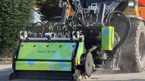 Multevo A JCB has a machine on the ground at the front which is green, yellow and blue and says 'Multevo'.