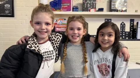 Three girls with their hair braided smiling at the camera. 