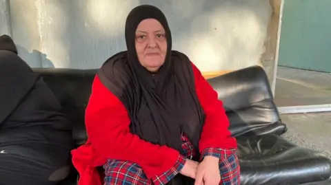 Alice Cuddy/BBC A Lebanese woman wearing a red cardigan sits on a black couch